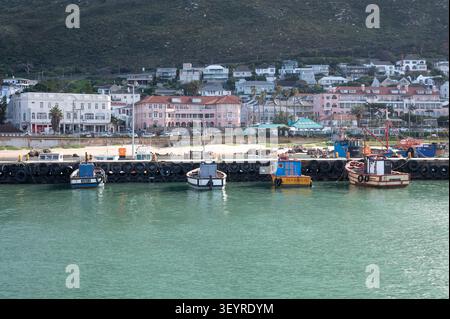 Plusieurs bateaux de pêche colorés sont amarrés le long d'une jetée du port bordée de pare-chocs en pneus, avec une ville côtière pittoresque aux bâtiments aux teintes pastel Banque D'Images