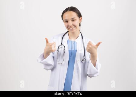 Jeune médecin féminin donnant des pouces vers le haut signe dans un studio photo professionnel envi... Banque D'Images