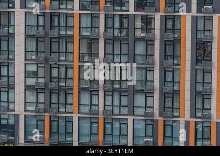 Bâtiment moderne de plusieurs étages doté d'une grille de fenêtres encadrées de panneaux verticaux gris foncé ou noir orange et blanc ajoutant un contraste, rectangulaire ai Banque D'Images