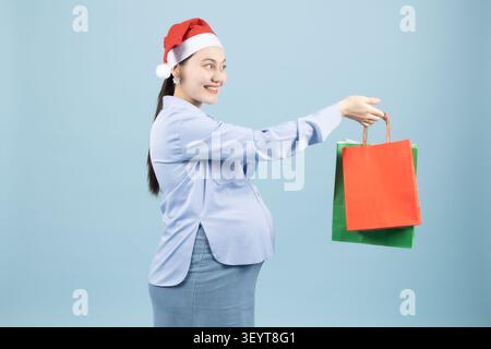 Femme enceinte dans le chapeau de santa tenant des sacs à provisions dans une photo professionnelle stu... Banque D'Images
