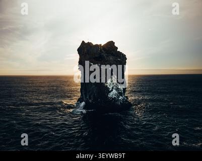 Vue aérienne de Haystack Rock s'élevant de l'océan Pacifique au coucher du soleil, avec des eaux sombres et une lumière dorée se reflétant sur la surface, Cannon Beach, Orego Banque D'Images
