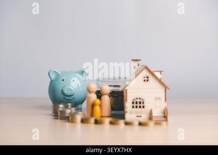 Tirelire bleue avec figurines familiales en bois, pot d'argent, pièces de monnaie et modèle de maison, représentant l'épargne de la maison familiale, fonds de versement initial, planification hypothécaire, Banque D'Images