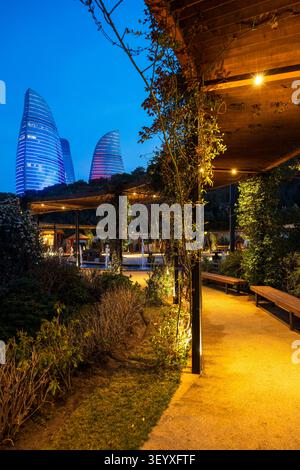 Passerelle de pergola illuminée avec des plantes grimpantes dans le parc de Chambarakand avec deux Flame Towers qui brillent à l'heure bleue. Bakou, Azerbaïdjan. Banque D'Images