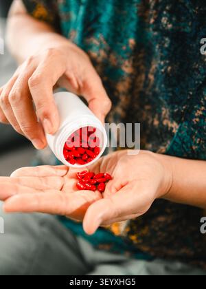 Gros plan de femme asiatique versant des pilules rouges de la bouteille de médecine dans la main à la maison, concept de soins de santé, médicaments, supplément, traitement, bien-être, Banque D'Images