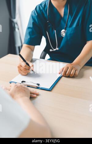 Professionnel de la santé dans les gommages bleus écrivant des notes médicales sur le presse-papiers pendant la consultation du patient, la visite clinique, le bilan de santé, le diagnostic, et PA Banque D'Images