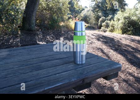 Une photographie en gros plan d'une bouteille isotherme moderne en acier inoxydable avec une poignée texturée vert citron vif reposant sur les planches de bois usées d'un pique-nique Banque D'Images