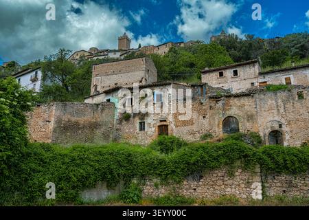 Le village de Capestrano présente d'anciennes maisons en pierre sur une colline, couvertes de végétation, et une tour historique visible sous un ciel nuageux. Abruzzes Banque D'Images