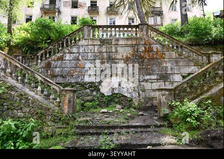 Un escalier en pierre recouvert de mousse avec des balustrades ornées mène à un bâtiment abandonné entouré de forêt envahie par la végétation dans la ville fantôme de Tkuarchal, A Banque D'Images