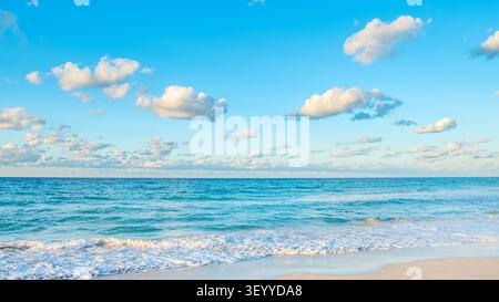 Vagues de l'océan sereines lançant doucement la plage de sable sous un ciel bleu vif rempli de nuages/ Banque D'Images