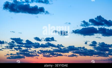 Ciel coloré de coucher de soleil avec des nuages dispersés sur un horizon au crépuscule près d'un paysage tranquille. Banque D'Images