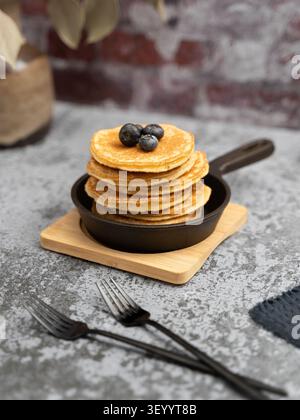 Petit-déjeuner rustique composé de crêpes moelleuses recouvertes de myrtilles et servies dans une poêle en fonte Banque D'Images