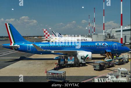 Fiumicino, Italie - 19 juillet 2026 : Airbus A220-300 d'ITA Airways en livrée bleue stationné à l'aéroport avec des véhicules de service au sol et d'autres avions Banque D'Images