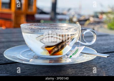 Tasse de thé noir Pickwick servi dans une tasse en verre transparent sur une soucoupe transparente Banque D'Images