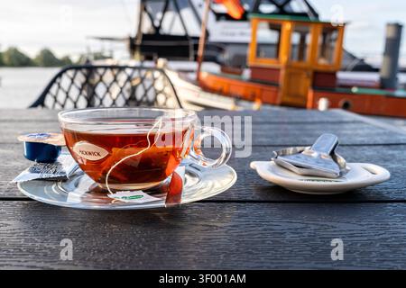 Tasse de thé noir Pickwick servi dans une tasse en verre transparent sur une soucoupe transparente Banque D'Images