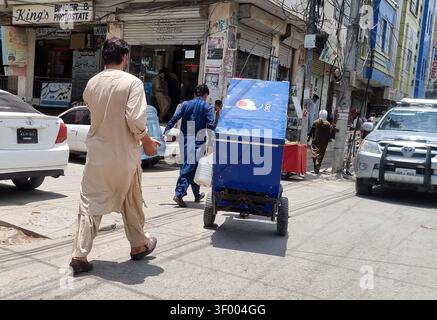 QUETTA, PAKISTAN - 05 juillet 2026 : un ouvrier a emprunté la route animée de Quetta le 5 juillet 2026, transportant un congélateur sur un chariot à main pour réparation. Cette scène souligne le dynamisme du commerce quotidien de la ville, où les vêtements traditionnels et les entreprises locales prospèrent au milieu de boutiques à plusieurs étages et d'activités de rue animées. La région, caractérisée par son réseau complexe de câbles électriques et la présence de véhicules divers, reflète l'environnement économique dynamique de l'Asie du Sud. Ces activités mettent en évidence la résilience et l'esprit d'industrialisation qui prévalent dans les communautés urbaines pakistanaises. (Sami Kh Banque D'Images
