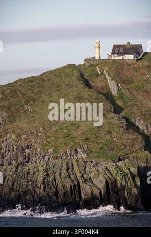 Un phare et un bâtiment se dressent au sommet d'une colline herbeuse surplombant l'océan, avec des falaises rocheuses menant à l'eau. Banque D'Images