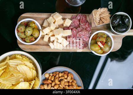 Vue de haut en bas d'une planche de charcuterie servie dans un jardin en été, avec des morceaux de cheddar tranchant, du salami tranché et des olives marinées Banque D'Images