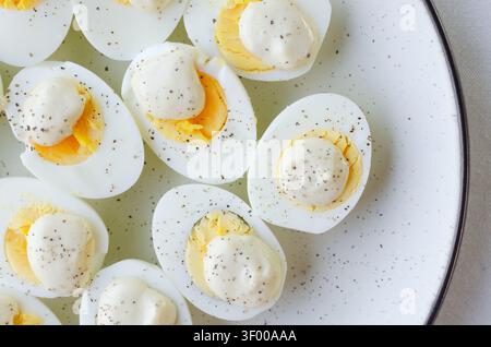 Une assiette avec des moitiés d'oeufs durs, décorée de sauce blanche et de poivre noir. Une présentation minimaliste propre qui crée une image élégante d'un simple Banque D'Images