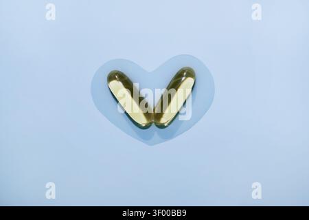 Deux softgels d'huile de poisson créant une forme de coeur sur fond bleu pastel Banque D'Images