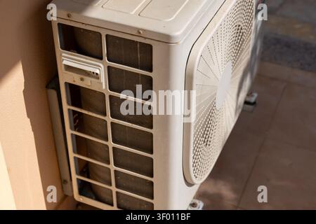 Vue rapprochée d'une unité de climatisation extérieure, mettant en évidence les serpentins du condenseur poussiéreux et la grille du ventilateur, montés sur un mur Banque D'Images