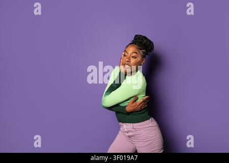 Danseuse afro urbaine confiante en streetwear élégant posant avec les bras croisés contre un mur de studio violet, exprimant le rythme, l'attitude et la modernité Banque D'Images
