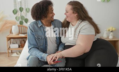Femme et homme tenant un smartphone, la femme pose la main sur son genou, puis se penche pour un câlin dans une chambre à coucher ; affection chaleureuse. Banque D'Images