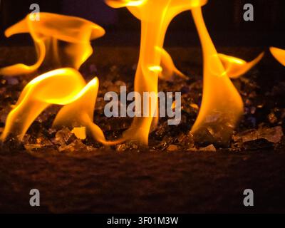 Gros plan abstrait de flammes de feu orange dansantes sur verre de feu décoratif en fond sombre Banque D'Images