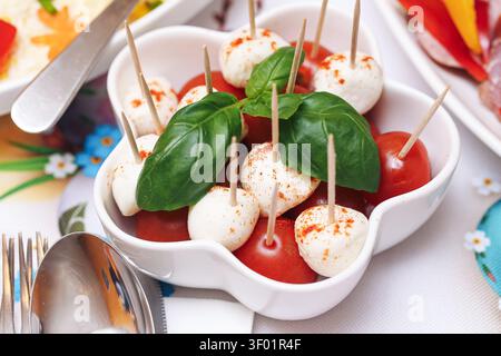 Häppchen de mozzarella et tomates cerises sur des brochettes en bois avec du basilic frais. Fond de finger food pour réception de buffet de fête et catering Banque D'Images