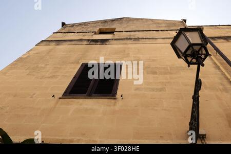 Regardant vers le haut un bâtiment en pierre vieillie avec des volets fermés foncés et un lampadaire ornemental contre un ciel clair. Italie, lecce, 18 juillet 2025 Banque D'Images