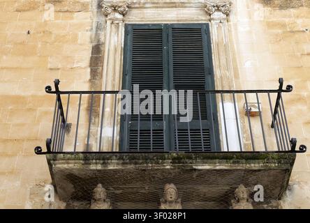 Balcon historique en pierre baroque décoré de caryatides et d'une balustrade en fer forgé ornée, avec volets fermés en bois vert. Italie, lecce, 18 juillet Banque D'Images