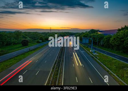 Longue exposition de traînées de lumière de véhicule sur une autoroute M4 à plusieurs voies au coucher du soleil avec un ciel orange horizon et des arbres verts, Royaume-Uni. JCT 13 Banque D'Images