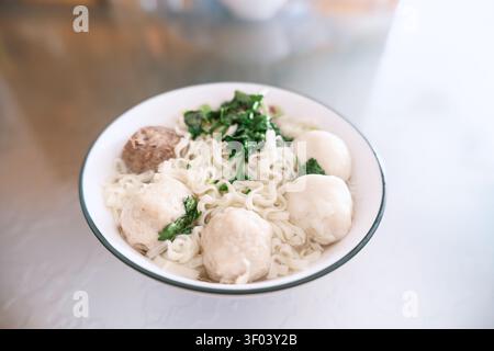 Mie Ayam indonésien avec boulettes de viande de poulet et herbes fraîches dans un bol blanc, nourriture de rue traditionnelle Banque D'Images