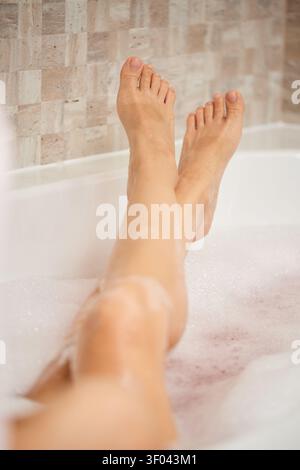 Femme profitant d'un bain moussant apaisant, ses jambes et ses pieds visibles au-dessus de l'eau dans un moment de soin personnel et de détente Banque D'Images