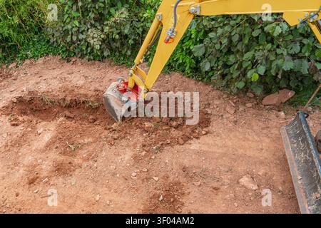 Gros plan d'un godet de mini-pelle jaune creusant dans un sol brun sec pour créer une ligne de tranchée. Travaux professionnels de terrassement et d'aménagement paysager sur un Banque D'Images