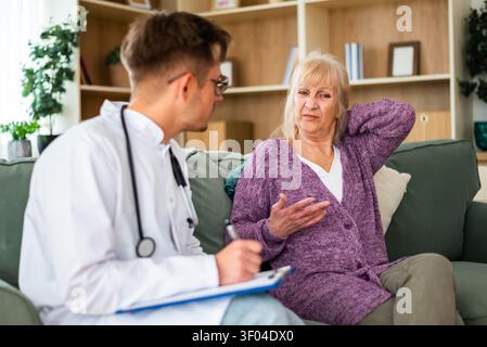 Une femme âgée décrit une gêne dans le cou et l'épaule en parlant avec un professionnel de la santé lors d'une visite à domicile. Banque D'Images