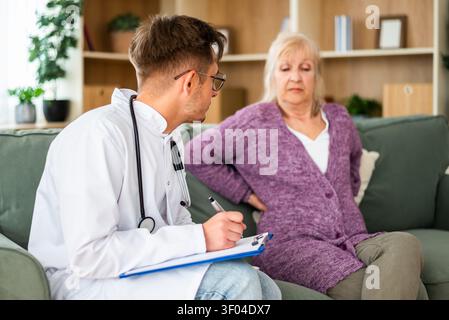 Une femme âgée décrit une gêne dans son dos en parlant avec un professionnel de la santé lors d'une visite à domicile. Banque D'Images