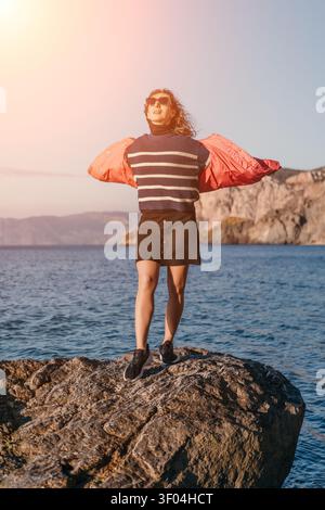 Femme coucher de soleil océan debout sur un rocher côtier avec les bras tendus pendant un coucher de soleil doré au bord de la mer Banque D'Images
