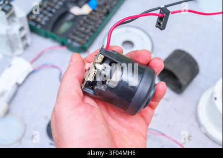 Main tenant un moteur électrique démonté avec des fils exposés et une carte de circuit imprimé pour réparation. Banque D'Images