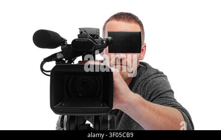 Un caméraman professionnel regarde directement dans l'objectif tout en faisant fonctionner une caméra vidéo sur un trépied sur un fond blanc. Banque D'Images