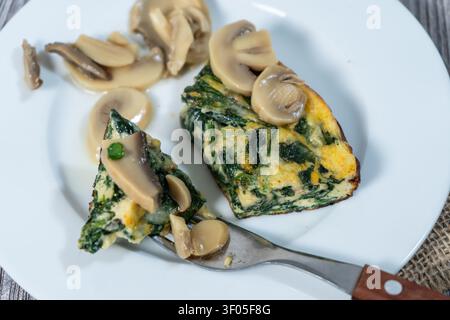 Morceaux de frittata aux épinards servis avec des champignons tranchés sur une assiette blanche, offrant un repas sain et riche en protéines Banque D'Images