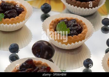 Tartes aux fruits maison remplies de confiture de baies riches, stylisées avec une prune fraîche et des myrtilles sur une surface réfléchissante, parfaites pour la boulangerie, le dessert, la pâtisserie Banque D'Images