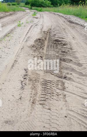 Traces de pneus profondes sur une route sablonneuse sèche. Les marques de profil texturées des pneus de voiture recouvrent la surface argilo-sableuse inégale d'une route rurale. Banque D'Images