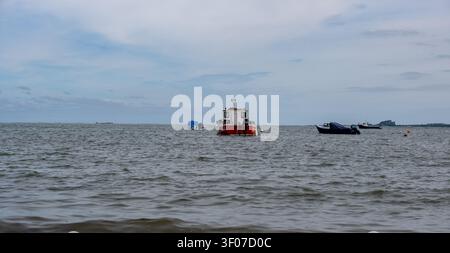 Des bateaux amarrés sur les eaux agitées au large de l'île sainte, côte de Northumberland, se balançant contre les vagues sous une mer dramatique et ridée par le vent. Banque D'Images
