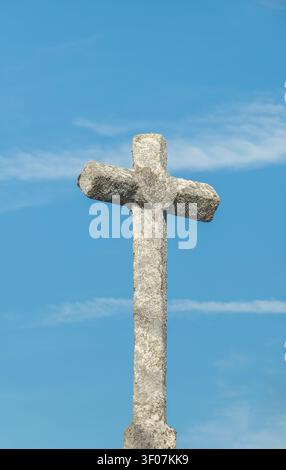 Ancienne croix chrétienne en granit debout sous un ciel bleu éclatant avec de fins filaments de nuages, gros plan Banque D'Images