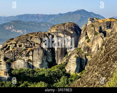 Kalambaka, Grèce – 24 juillet 2024 : groupe de monastères Meteora. Un groupe de rochers escarpés avec des grottes. Feuillage vert au premier plan. Ciel bleu. Chaîne de montagnes o Banque D'Images