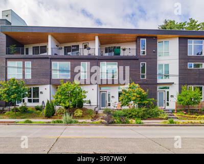 Complexe d'appartements contemporains décoré d'un parement en bois sombre, de touches blanches et de grandes fenêtres avec vue sur la rue et sur la cour avant aménagée. Banque D'Images