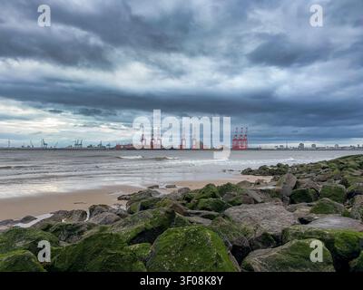Plage de New Brighton avec des rochers couverts d'algues faisant face aux grues portuaires de Liverpool de l'autre côté de la rivière Mersey Banque D'Images