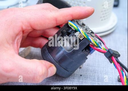 Main tenant un moteur électronique sale avec des fils et une carte circuit exposés pendant la maintenance. Banque D'Images