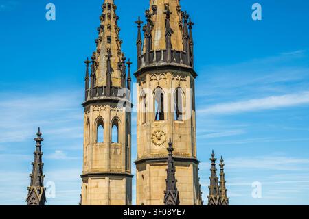 Tours d'église gothiques avec flèches et horloge contre un ciel bleu éclatant, gros plan détaillé de l'architecture historique de la cathédrale Banque D'Images