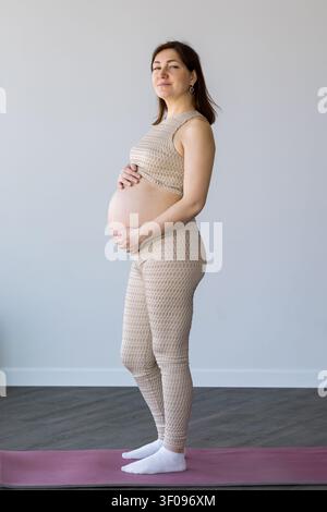 Femme enceinte debout sur un tapis de yoga en touchant son ventre Banque D'Images
